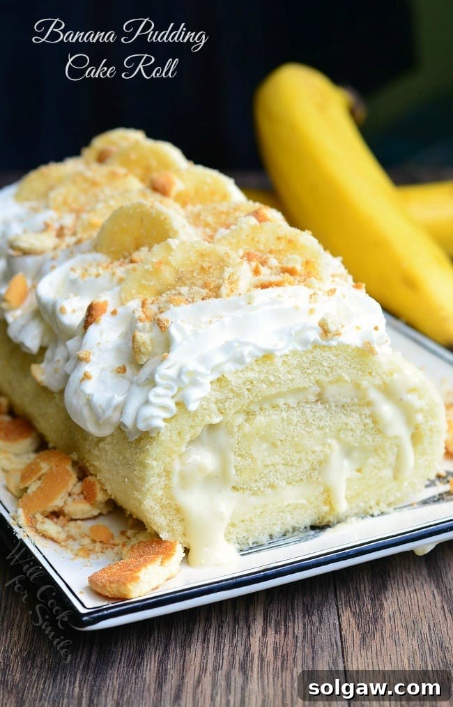Banana pudding cake roll on a decorative white rectangular plate on a wooden table with 2 bananas in the background