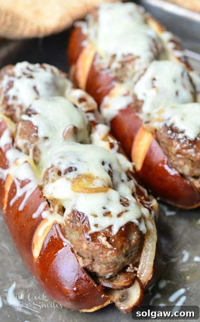 A perfectly assembled Bacon Buffalo Meatball Sub, featuring sliced pretzel roll, juicy meatballs, sauteed vegetables, and melted mozzarella cheese.