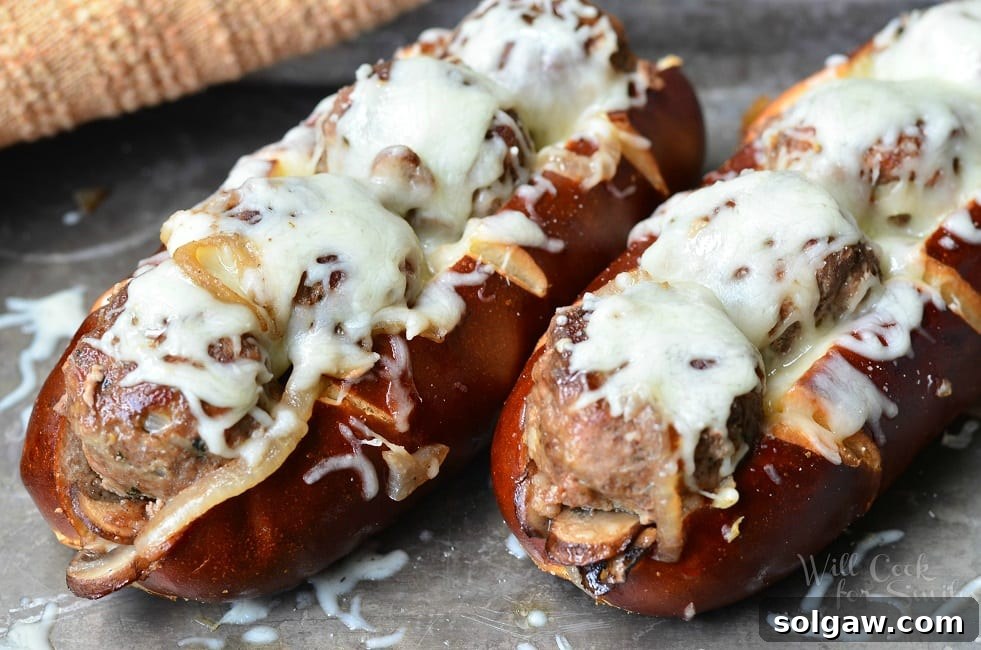 A close-up shot of a prepared Bacon Buffalo Meatball Sub, showcasing the juicy meatballs, sautéed veggies, and melted mozzarella cheese inside a pretzel bun.