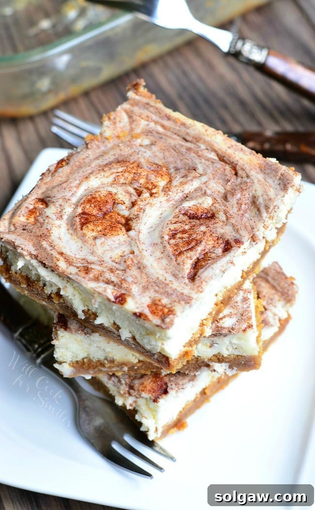 Several Caramel Cinnamon Swirl Cheesecake Bars are stacked on a small, white plate. A fork lays on the plate as well.