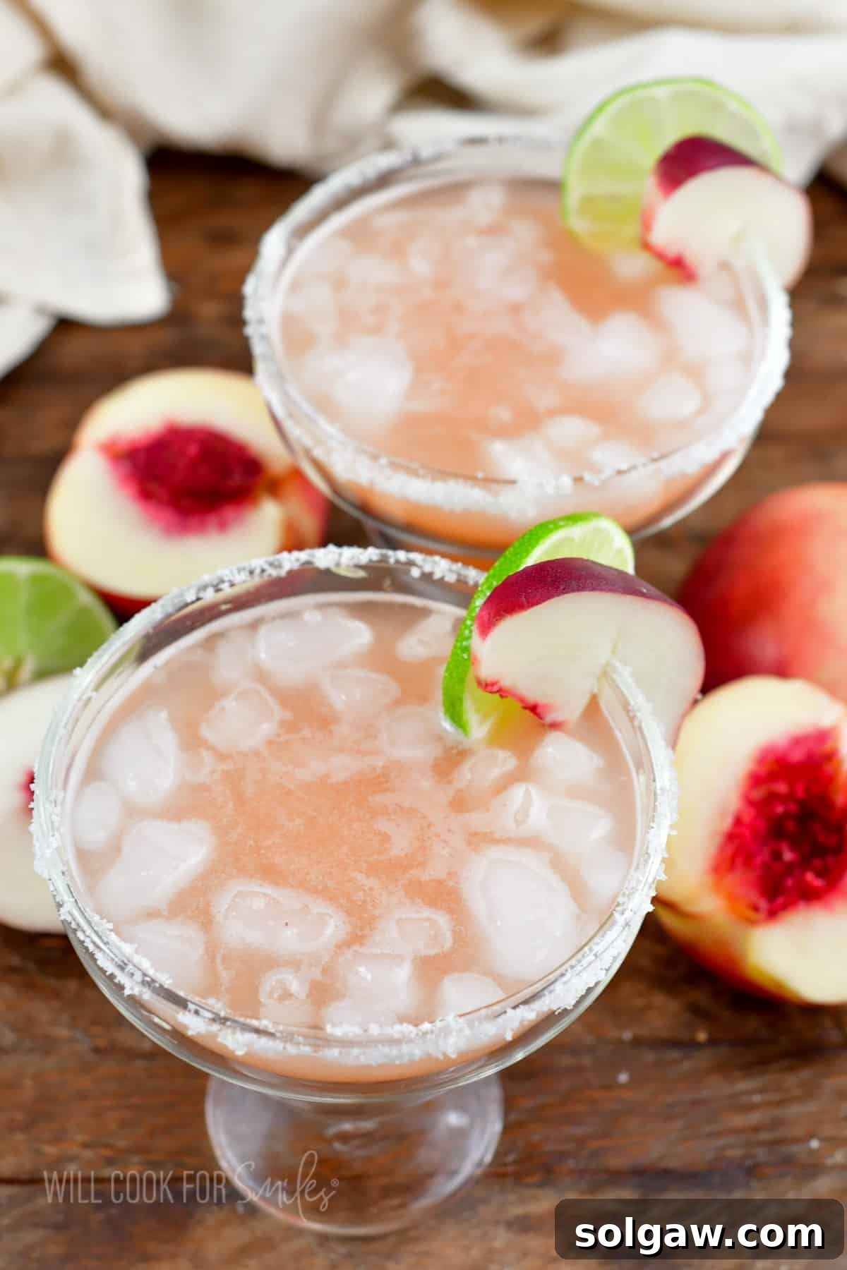 Two margarita glasses are filled with a luscious peach margarita mixture and ice, ready to be enjoyed.